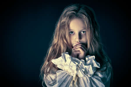 Scary little girl ghost in a white nightgown folded her hands in prayer. Black background. Halloween.の写真素材