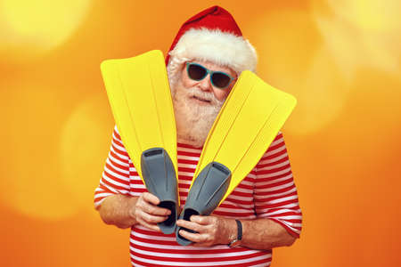Jolly funny Santa Claus goes on vacation to the sea. Christmas Holidays, tourist trips to hot tropical countries. Bright yellow background. Copy space.の写真素材