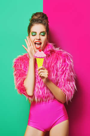 Stunning fashionable model posing in colorful clothes with paper ice cream on a vivid green and fuchsia background. Active bright lifestyle. Copy space.の写真素材