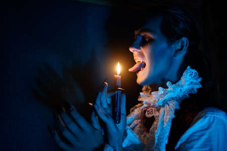 Scary vampire grins at a candle sneaking around the castle in the night in search of a victim. 19th century style. Halloween.の写真素材