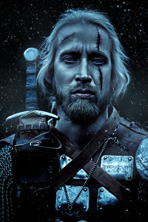 Portrait of a brave medieval warrior in armor with a sword on a snowy background. The Witcher man.