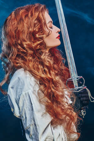 Profile portrait of a beautiful and brave red-haired woman with a battle epee (rapier). Historical reconstruction of the 16-17th centuries.の写真素材