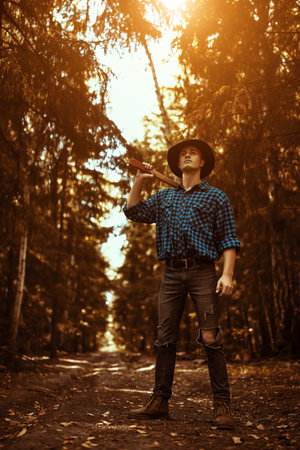 Full length portrait of a handsome strong man lumberjack with an ax in the wild forest.