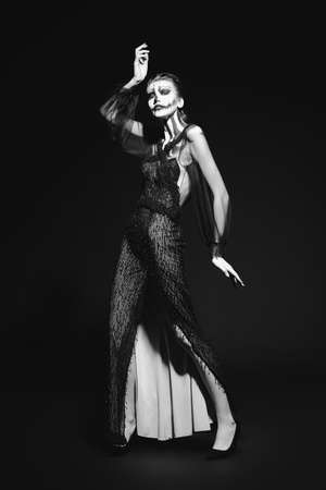 Full length monochrome portrait of a beautiful graceful woman with pumpkin skull makeup over black background. Halloween. Day of The Dead.の写真素材