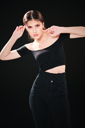 Portrait of an attractive brunette dancer girl with bright make-up posing at studio in black clothes...