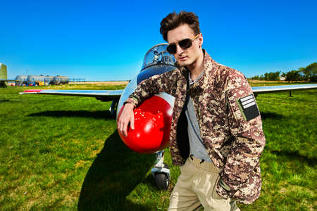 Handsome man pilot wearing military uniform stands by his fighter jet at the airfield. Military aircraft.の写真素材