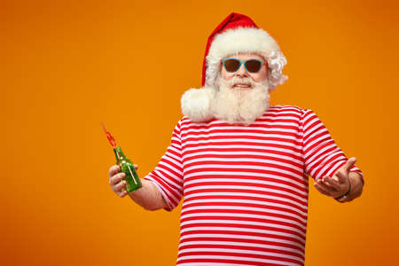 Santa Claus in a red hat and sunglasses holding a bottle of drink on a yellow background. Christmas Holidays, tourist trips to the sea. Bright yellow background.の写真素材