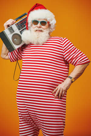 Cool DJ Santa Claus in sunglasses holds tape recorder on a festive background with lights. Christmas songs and music. New Year party.の写真素材