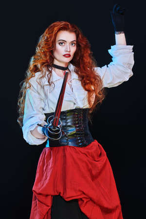 Portrait of a beautiful red-haired girl with a battle epee (rapier) on a black background. Historical reconstruction of the 16-17th centuries.の写真素材