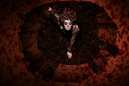 Scary and beautiful Calavera Catrina looking up at camera over dark red background. Fashion model...