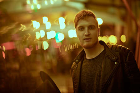 Night life in a big city. Modern young man walks along a city street lit by night lights.の写真素材