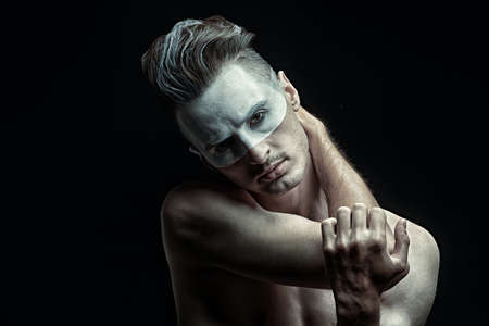 Art portrait of a calm handsome man with white paint on his face standing on a black background. Copy space. Male beauty. Make-up and hairstyle.の写真素材