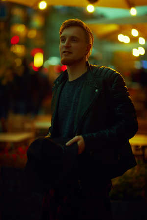 Hipster young man walks along a city street lit by night lights. Night life in a big city.の写真素材