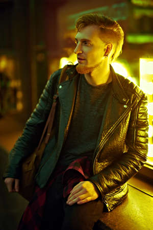 Night life in a big city. Modern young man walks along a city street lit by night lights.の写真素材