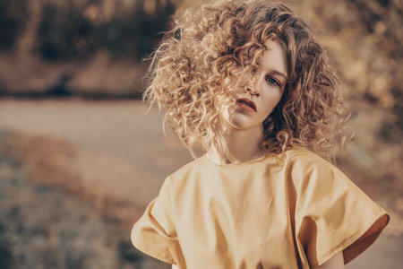 A portrait of a charming young girl with curly fair hair in a yellow dress. Fashion, beauty.