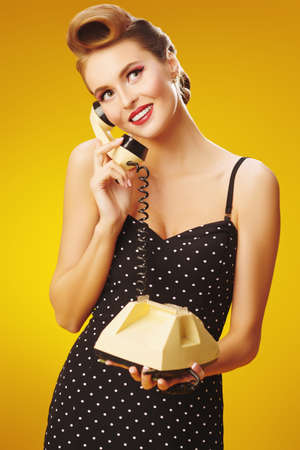 Portrait of a charming pin-up woman talking on the phone on a yellow background. Beauty, fashion concept.の写真素材