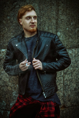 Hipster young man posing with cigarette against a stone wall. Night life in a big city.