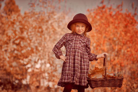 Autumn. Little girl walks through a beautiful autumn park and collects leaves fallen from trees. Retro style. Children's fashion.の写真素材