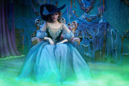 Charming woman witch in a hat and beautiful dress sitting in a vintage armchair in the old castle....