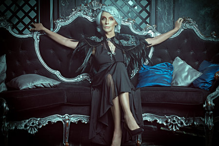 A beautiful old woman, a noble widow with gray hair and a rich black dress, lies on a vintage sofa...