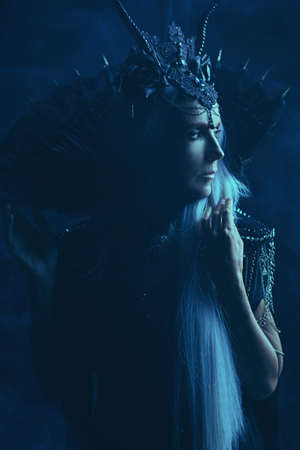 A portrait of a stately and beautiful old woman with long gray hair, in a rich headdress and a rich black dress against a dark background. Black Queen, Witch. Halloween.の写真素材