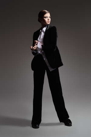Fashion concept. Full length portrait of a gorgeous graceful young woman model posing in motion in black velvet suit and white shirt on a gray background.の写真素材
