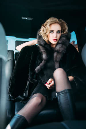 A portrait of a gorgeous blonde lady posing in a car. Car, fashion, beauty, chic.の写真素材