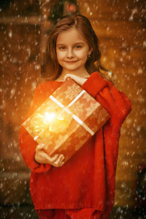 Merry Christmas and Happy New Year! Pretty little girl holds Christmas gift in a house beautifully decorated with spruce garlands and New Year's toys.の写真素材