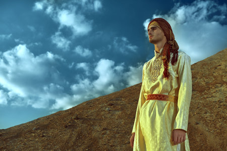 Portrait of a handsome young man in national Indian costume in the desert at sunset. Men's beauty,...