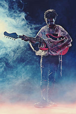 Halloween party. Scary zombie boy teenager plays electric guitar in the smoke.の写真素材