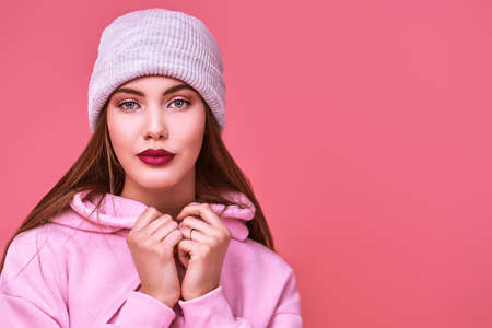 Youth fashion. Modern teen girl in a pink sweatshirt and a hat posing at studio on a pink background. Cosmetics and make-up. Copy space.の写真素材