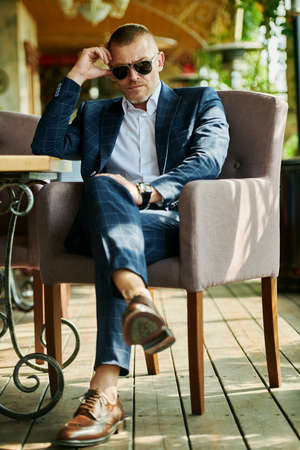 Handsome mature man in an elegant classic suit having a rest on the summer terrace. Male fashion. Optics, sunglasses for men. Summer vacation.の写真素材