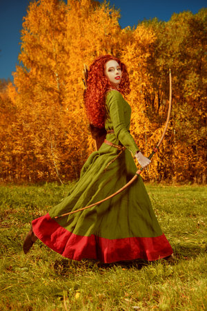 A beautiful red-haired girl archer of the Middle Ages runs through the meadow. Celtic culture....