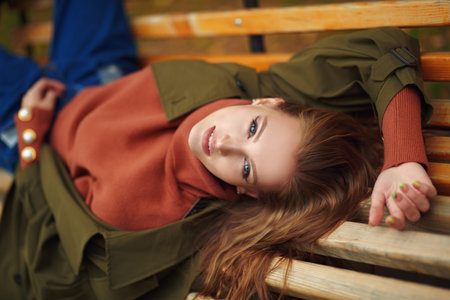 Happy girl resting carefree on a bench in a beautiful autumn park, leaf fall. Autumn mood.