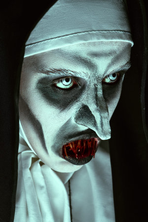 Close-up portrait of a devilish scary nun with bloody teeth. Halloween and Horrors.