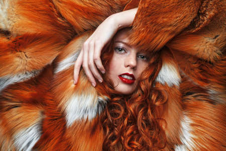 Fur coat style. Portrait of a beautiful sensual woman with red hair in a luxurious fox fur coat. Winter beauty fashion.の写真素材