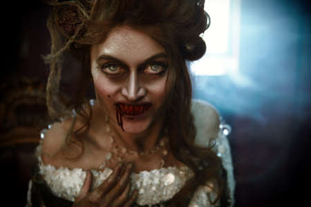 Halloween Close-up portrait of a bloodthirsty woman vampire in the old abandoned castle. Vintage style.の写真素材