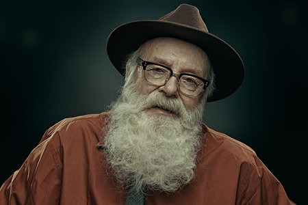 Portrait of a serious old man with long white beard wearing a hat and glasses and looking at camera....