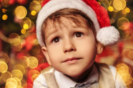 Dreamy little boy near the Christmas tree and looks into the camera with big eyes. Christmas and New Year concept.の写真素材