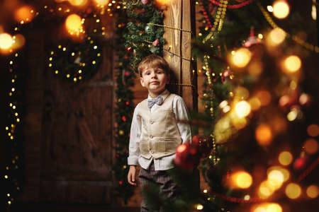 Happy little boy in elegant festive suit is standing in home decorated for Christmas. Merry Christmas and Happy New Year!の写真素材