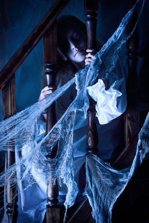 Little girl ghost in a nightgown wanders through the old house at night. Halloween.