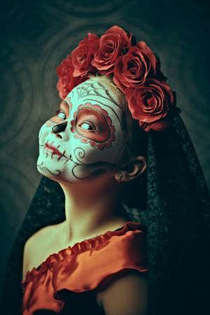 Side view portrait of a child girl in a costume of Calavera Catrina over dark background. Little girl with sugar skull makeup. Halloween. Dia de los muertos. Day of The Dead.の写真素材