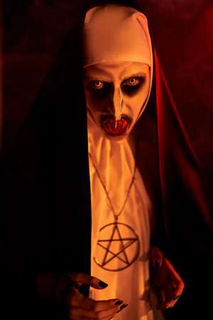 Portrait of evil cursed nun on a dark background in orange light. Halloween and Horrors.