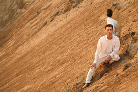 Handsome young man in white clothes is posing with a mirror in a desert. Men's fashion.の写真素材