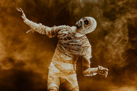 Evil mummy with burning eyes scares in yellow smoke against the dark background. Halloween. Ancient...