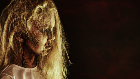 A close up portrait of a scary pale girl from horror film on black background. Zombie, halloween.