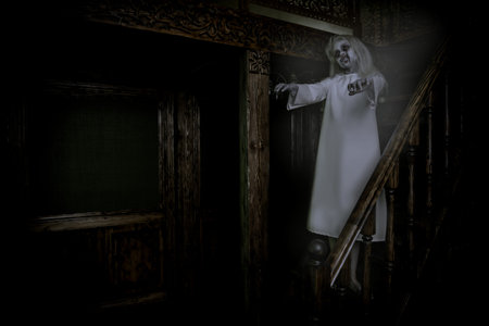 A full length portrait of a scary pale girl from a horror film in a room on the stairs. Zombie,...