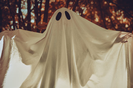 A ghost child under a white sheet with light inside in a dark forest. Halloween concept.