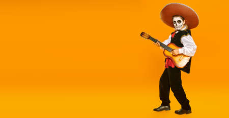 Handsome boy with sugar skull makeup plays the guitar over bright yellow background. Halloween. Dia de los muertos. Day of the dead. Copy space.の写真素材