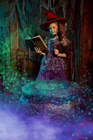 Cute happy child girl in a costume of a witch posing in an old house with Halloween decorations....